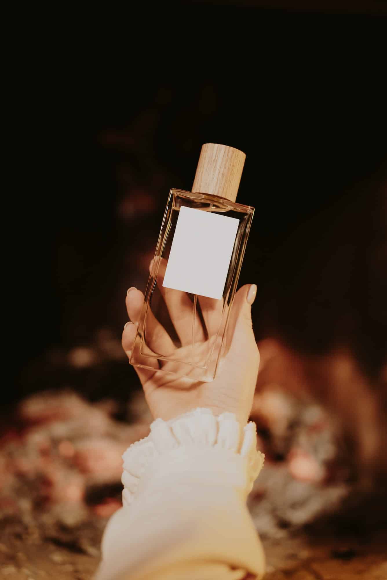 Beautiful minimalist parfume bottle in female hands on fireplace flame background.